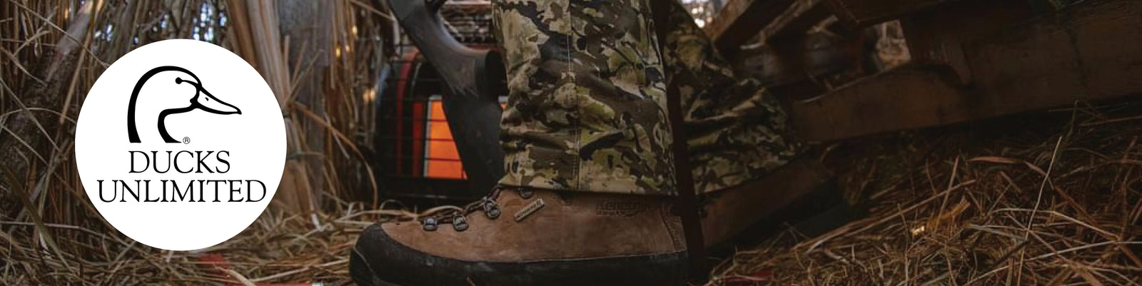 A close-up of a brown leather hunting boot with camouflage laces, shown in a rustic outdoor or hunting-themed setting with straw and wood. A white circular logo overlay on the left reads 'DUCKS UNLIMITED' with a duck silhouette.